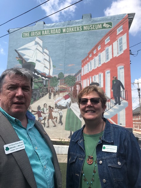 All Aboard! Michael Mellett and Cathy Reinholdt of the Irish Railroad Workers Museum in Baltimore in front of a period mural by Irish American artist Michel Harnett who included an African-American drayman, a profession in which many Free Blacks laboured. 